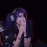 a woman with purple hair is wearing headphones and a black shirt .