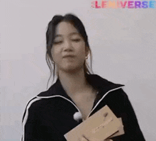 a woman in a black jacket is holding a box of chocolates .