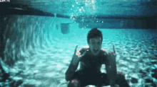 a man is sitting underwater in a swimming pool making a rock and roll sign .