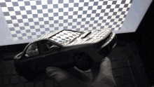 a person is holding a toy car in front of a checkered ceiling