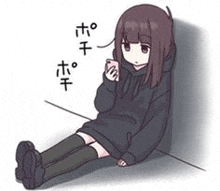 a girl in a black hoodie is sitting on the ground looking at her phone .