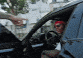 a man wearing sunglasses and a red headband is sitting in a car being handed something