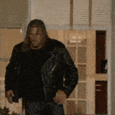 a man wearing a black leather jacket is standing in front of a window