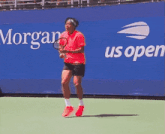 a man in a red shirt is kneeling on a tennis court with the number 13 behind him