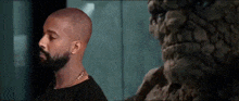 a bald man with a beard is standing next to a statue .