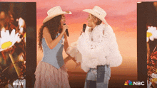 two women wearing cowboy hats singing into microphones in front of a sign that says nbc on it