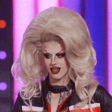 a drag queen with a very large blonde wig is wearing a red white and blue jacket