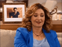 a woman in a blue jacket sits in front of a picture of a man