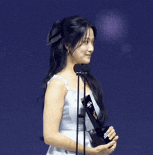 a woman in a white dress is holding a trophy in front of a microphone