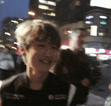 a blurry picture of a young man smiling in front of a city at night
