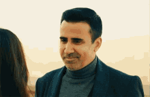a man in a suit and turtleneck is looking at a woman in a sweater .