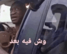 a man is sitting in the driver 's seat of a car with arabic writing on the window .