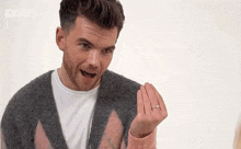 a man wearing a pink and gray sweater is holding something in his hand and making a funny face .
