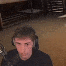 a young man wearing headphones is sitting in front of a microphone and looking at the camera .