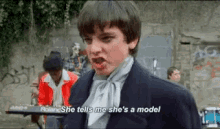 a young man in a suit and tie says she tells me she 's a model in a video .