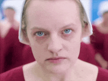 a close up of a woman 's face with blue eyes wearing a red shirt and a white headband .