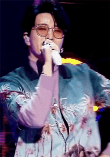 a man wearing glasses is singing into a microphone while wearing a blue jacket .