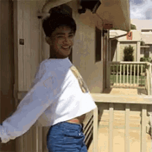 a young man wearing a crop top and jeans is standing on a balcony .
