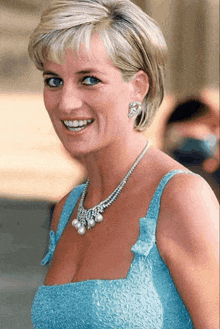 a woman in a blue dress and pearl necklace smiles