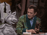a man in a green robe sits at a table with a stuffed pig
