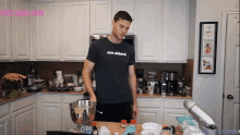 a man standing in a kitchen wearing a shirt that says man shlub