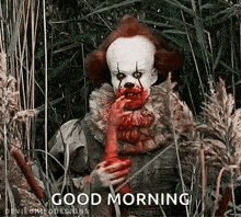 a clown with blood on his face is standing in a field of tall grass and holding a bloody hand .