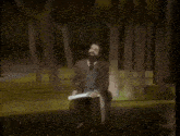 a man with a beard is sitting in front of a forest and says back to this one from that