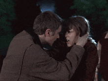 a man in a brown jacket holds a woman 's head