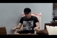 a man in a black hat is sitting in a chair holding a remote control .