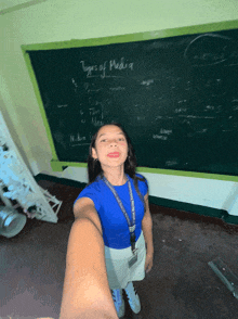 a girl taking a selfie in front of a chalkboard that says types of media