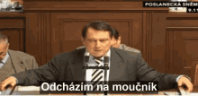 a man in a suit and tie is speaking into a microphone with the words " odchazim na moucnik " on the bottom