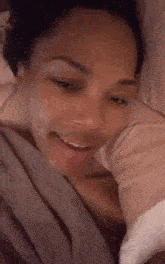 a woman is laying in a bed with a blanket on her head and smiling .