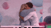 a man and a woman are hugging each other in a room with balloons .