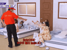 a man in a red shirt that says kiii kiii is pointing at a group of girls laying on beds