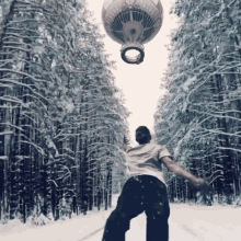 a man in a white shirt stands in a snowy forest with a hot air balloon in the background