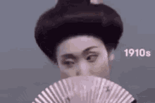 a geisha is holding a pink fan in front of her face .