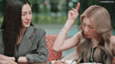 two women are sitting at a table with a plate of food and a watch on their wrists ..