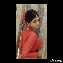 a woman wearing a red crop top and earrings is smiling while standing next to a tree .