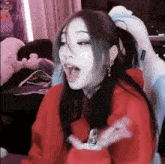 a girl in a red hoodie is sitting in a chair with her mouth open and making a funny face .