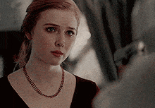 a woman with red hair wearing a necklace and a black top
