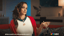 a woman is sitting on a couch holding a martini glass with nbc written on the bottom