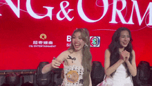 two women standing in front of a sign that says ' g & orm ' on it