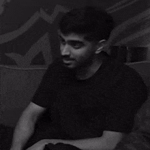 a man in a black shirt is sitting on a couch in a black and white photo