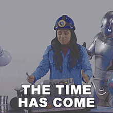 a woman in a blue lab coat is standing next to a robot with the words the time has come above her