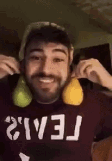 a man wearing a shirt that says tei12 is holding two pears in front of his face