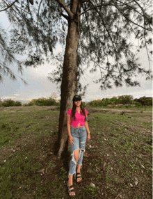 a woman in a pink shirt stands next to a tree in a field