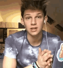 a young man wearing a tie dye shirt and headphones is sitting in front of a laptop computer .