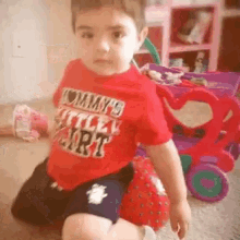 a little boy wearing a red shirt that says " tommy 's little tart "