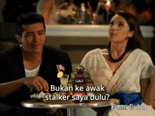 a man and a woman are sitting at a table and the man is asking the woman if she is a stalker