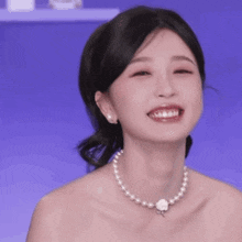 a woman wearing a pearl necklace is smiling .